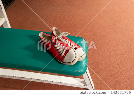 Red sneakers sit on a green bench in a room with a brown floor during daylight hours Red sneakers sit on a green bench in a room with a brown floor during daylight hours 142631799