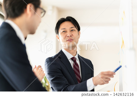 三個身穿西裝的男人正在開會,他們面帶微笑,使用著白板。 三個身穿西裝的男人正在開會,他們面帶微笑,使用著白板。 142632116