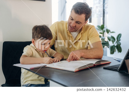 Father and young son studying together at a desk, reviewing a book with open pages, indoor setting featuring a plant and natural light from a window Father and young son studying together at a desk, reviewing a book with open pages, indoor setting featuring a plant and natural light from a window 142632432