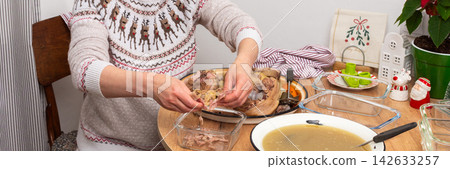 A woman separates boiled meat from bones to prepare kholodets, a jellied meat dish. She works at a wooden table with utensils and ingredients in a cozy kitchen during winter A woman separates boiled meat from bones to prepare kholodets, a jellied meat dish. She works at a wooden table with utensils and ingredients in a cozy kitchen during winter 142633257