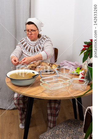 A woman separates boiled meat from bones to prepare kholodets, a jellied meat dish. She works at a wooden table with utensils and ingredients in a cozy kitchen during winter A woman separates boiled meat from bones to prepare kholodets, a jellied meat dish. She works at a wooden table with utensils and ingredients in a cozy kitchen during winter 142633260