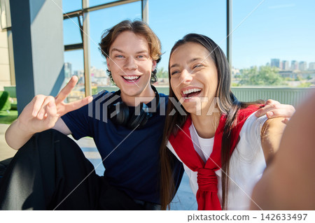 Two young university students taking selfie photo laughing showing victory sign near window Two young university students taking selfie photo laughing showing victory sign near window 142633497
