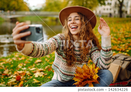 Stylish woman takes selfie on phone in autumn forest, communicates via video call. Concept of nature Stylish woman takes selfie on phone in autumn forest, communicates via video call. Concept of nature 142634226