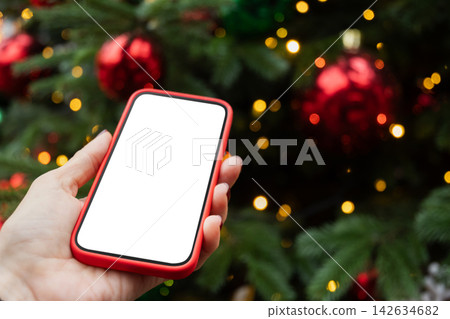 Smartphone with white screen in front of Christmas tree Smartphone with white screen in front of Christmas tree 142634682