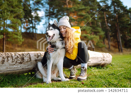 Woman with her husky dog walks in autumn forest. A cheerful pet spends time with its owner outdoors. 142634711