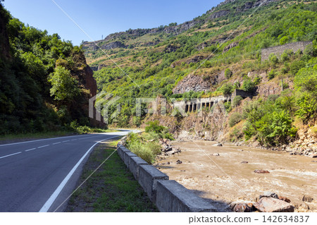 A winding asphalt road follows a muddy river. Armenia 142634837