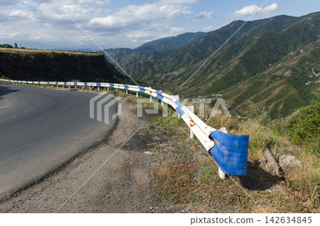 Mountain road hugs a cliff, protected by blue and white guardrails 142634845