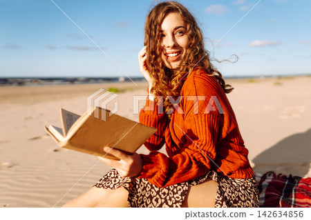 Woman reading book while lying on blanket during picnic. Concept of relaxation, solitude with nature Woman reading book while lying on blanket during picnic. Concept of relaxation, solitude with nature 142634856