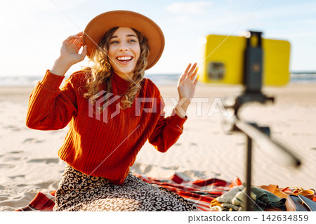 Style woman using smartphone with stabilizer, taking pictures in on sea beach. Woman creates content 142634859