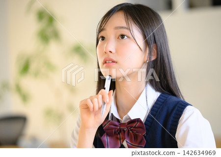 A high school girl holding a pen and thinking. A high school girl holding a pen and thinking. 142634969