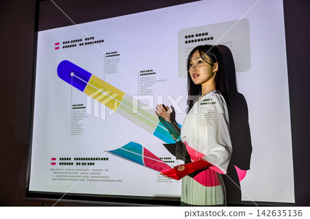 一位女士正在做演示,同時指著投影機上的資料。 一位女士正在做演示,同時指著投影機上的資料。 142635136