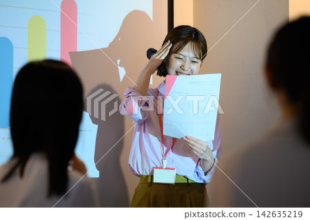 A female businessperson smiles and speaks while checking her presentation materials. A female businessperson smiles and speaks while checking her presentation materials. 142635219