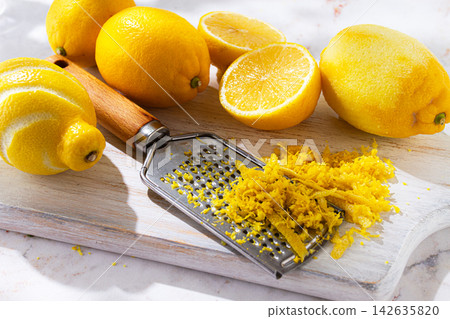 Fresh lemons on a cutting board with zest and lemon slices in a kitchen setting during daytime 142635820