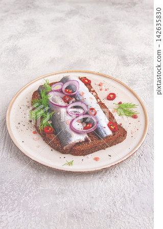 sandwiches , Herring fish, on dark rye bread, sprinkled with onion, chili pepper and herbs, on a light plate sandwiches , Herring fish, on dark rye bread, sprinkled with onion, chili pepper and herbs, on a light plate 142635830