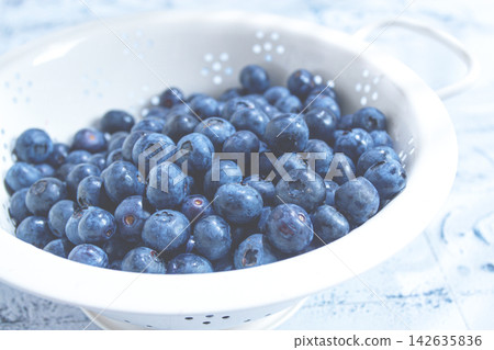 Fresh blueberries in a white colander on a blue surface with water droplets Fresh blueberries in a white colander on a blue surface with water droplets 142635836