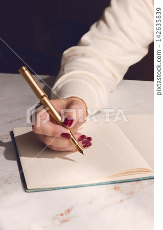 A woman writes with an ink fountain pen, in a notebook, at a wooden table, natural light, A woman writes with an ink fountain pen, in a notebook, at a wooden table, natural light, 142635839