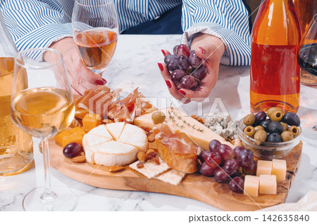 Sharing a platter of cheese, meats, olives, and grapes with drinks on a table during a social gathering Sharing a platter of cheese, meats, olives, and grapes with drinks on a table during a social gathering 142635840