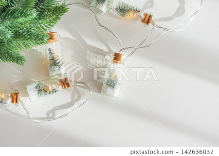 Festive miniature pine trees inside glass bottle string lights on white background with pine branch Festive miniature pine trees inside glass bottle string lights on white background with pine branch 142636032