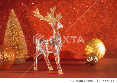 Elegant crystal reindeer figurine with golden Christmas tree and ornaments on red sparkling background Elegant crystal reindeer figurine with golden Christmas tree and ornaments on red sparkling background 142636033