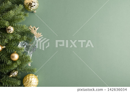Christmas fir branch with golden ornaments and clear reindeer decoration on green background 142636034