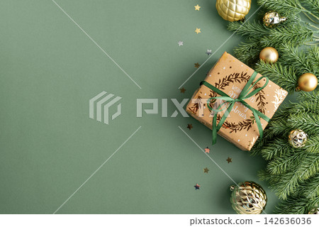 Festive Christmas gift box with ornaments and fir branches arranged on a green background celebrating holiday season joy 142636036