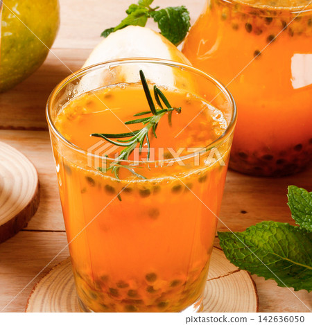 Fresh passion fruit juice served in a glass with pulp and rosemary, accompanied by fresh fruit on a rustic table. Fresh passion fruit juice served in a glass with pulp and rosemary, accompanied by fresh fruit on a rustic table. 142636050