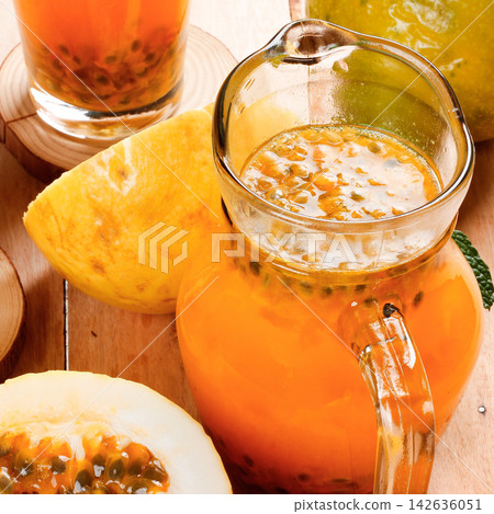 Refreshing tropical drink made with passion fruit, served in a pitcher and a glass, accompanied by whole and cut fruit on a rustic wooden table. Refreshing tropical drink made with passion fruit, served in a pitcher and a glass, accompanied by whole and cut fruit on a rustic wooden table. 142636051