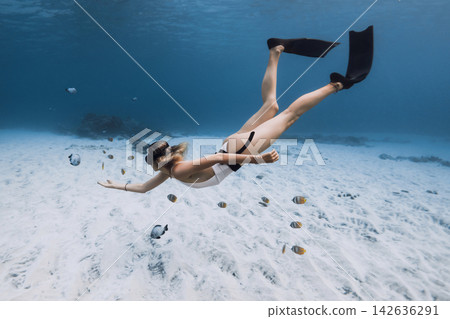 Female free diver swimming over a sandy seabed in clear tropical ocean water 142636291