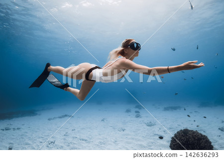 Woman freediver gliding gracefully over a sandy ocean floor in clear blue water Woman freediver gliding gracefully over a sandy ocean floor in clear blue water 142636293