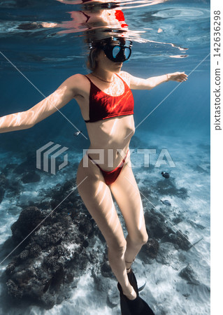 Woman free diver in red bikini swimming underwater above a rocky coral reef Woman free diver in red bikini swimming underwater above a rocky coral reef 142636298