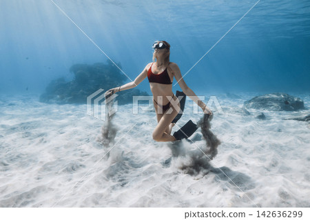 Female free diver swimming underwater with sand in hands Female free diver swimming underwater with sand in hands 142636299