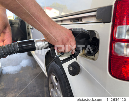 Person refueling a car at a gas station amid rising fuel prices 142636420