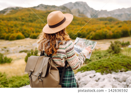 Female trekker studying map. Young woman hiking in autumn landscape with map. Travel, nature concept Female trekker studying map. Young woman hiking in autumn landscape with map. Travel, nature concept 142636592