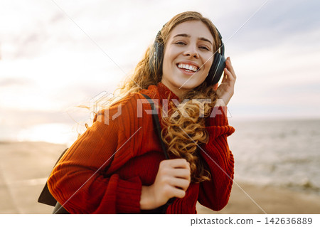 Portrait of beautiful young girl enjoying freedom listening to music against the backdrop of the sea 142636889