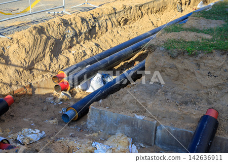 Insulated industrial pipes in a ground trench covered with sand and soil. Municipal engineering, energy supply maintenance 142636911
