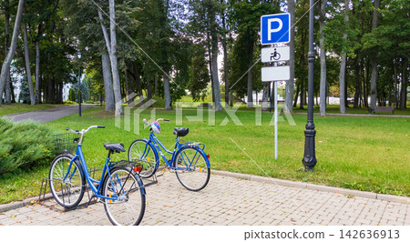 Blue City Bicycles Standing in Bike Rack near Parking Sign on Paved Area. Eco Travel Concept Blue City Bicycles Standing in Bike Rack near Parking Sign on Paved Area. Eco Travel Concept 142636913