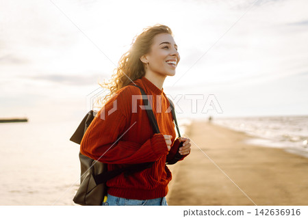 Young woman enjoying a breezy day near a vibrant red lighthouse. Autumn sunset Young woman enjoying a breezy day near a vibrant red lighthouse. Autumn sunset 142636916