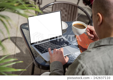 Man working on laptop and drinking coffee at outdoor cafe Man working on laptop and drinking coffee at outdoor cafe 142637110