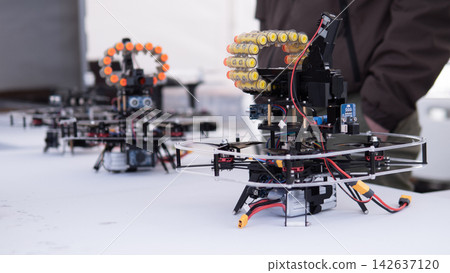 Two homemade quadcopter drone prototypes with transparent frames and visible wiring sit on white tabletop, highlighting testing and robotics hardware details against soft blurred background 142637120
