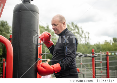 Mature boxer training with heavy punching bag outdoors Mature boxer training with heavy punching bag outdoors 142637147