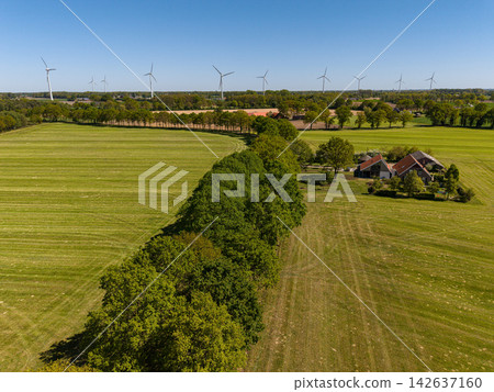 High angle wide horizontal aerial drone photograph of wind turbines, traditional farmstead, tree lines, and green pastures in rural Gelderland, Achterhoek, Netherlands on sunny spring day High angle wide horizontal aerial drone photograph of wind turbines, traditional farmstead, tree lines, and green pastures in rural Gelderland, Achterhoek, Netherlands on sunny spring day 142637160