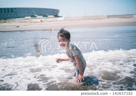 A boy laughing, his clothes still wet at the water's edge of the summer sea. A boy laughing, his clothes still wet at the water's edge of the summer sea. 142637182