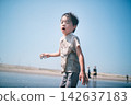 A boy covered in mud picking up seashells turns around on a summer tidal flat. 142637183