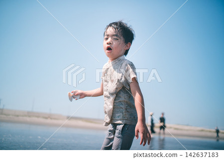 A boy covered in mud picking up seashells turns around on a summer tidal flat. A boy covered in mud picking up seashells turns around on a summer tidal flat. 142637183