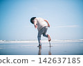 A boy plays barefoot at the water's edge on a summer beach, lifting one leg. 142637185