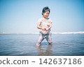 A boy laughing as he picks up seashells in the shallow waters of the summer sea. 142637186