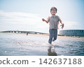 A boy walks and plays in the shallow waters of the summer sea fully clothed. 142637188