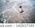 The back view of a child playing on their stomach at the water's edge of a summer beach. 142637189