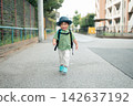 A boy with a hat and backpack walks down a residential street with a smile on his face. 142637192