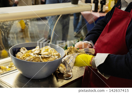 Seafood vendor preparing fresh oysters in bustling market environment Seafood vendor preparing fresh oysters in bustling market environment 142637415